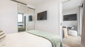 A modern bedroom with a bed, a television mounted on the wall, and a sliding door leading to a bathroom. - Marco Panoramic Skyline Escape with Pool and Gym (Southbank)