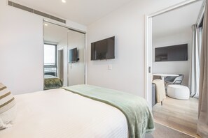 Ein modernes Schlafzimmer mit einem Bett, einem an der Wand montierten Fernseher und einer Schiebetür zu einem Badezimmer.