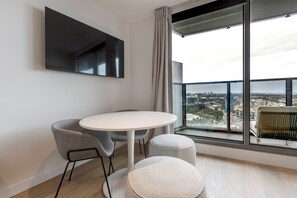 A modern room with a round table, two chairs, a sofa, and a large window offering a city view. - Marco Panoramic Skyline Escape with Pool and Gym (Southbank)