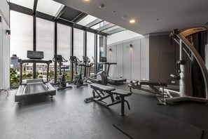 Ein Fitnessstudio mit verschiedenen Trainingsgeräten, großen Fenstern und Blick auf die Stadt.