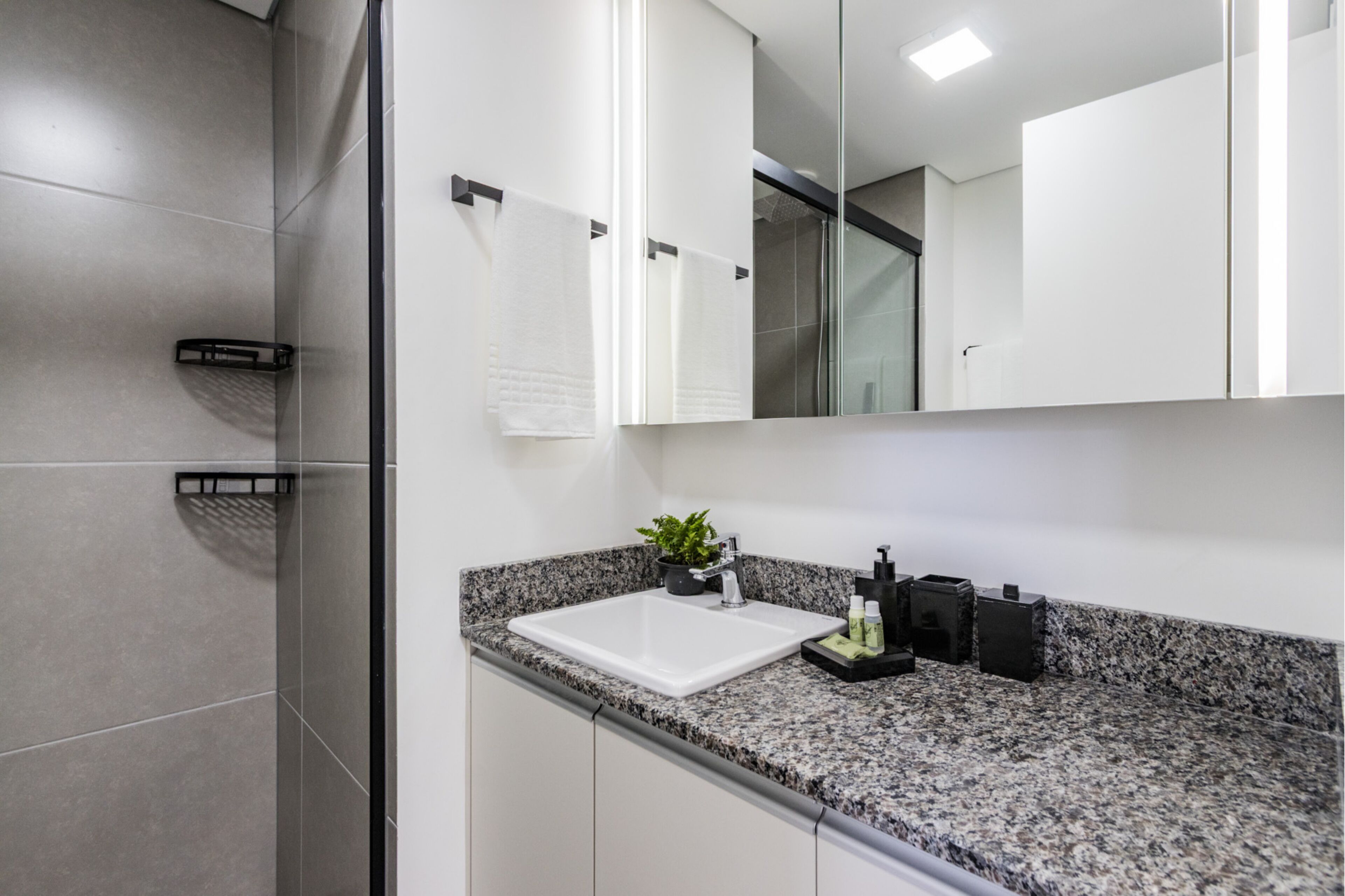 Un baño moderno con encimera de granito, un lavabo blanco y un espejo encima.