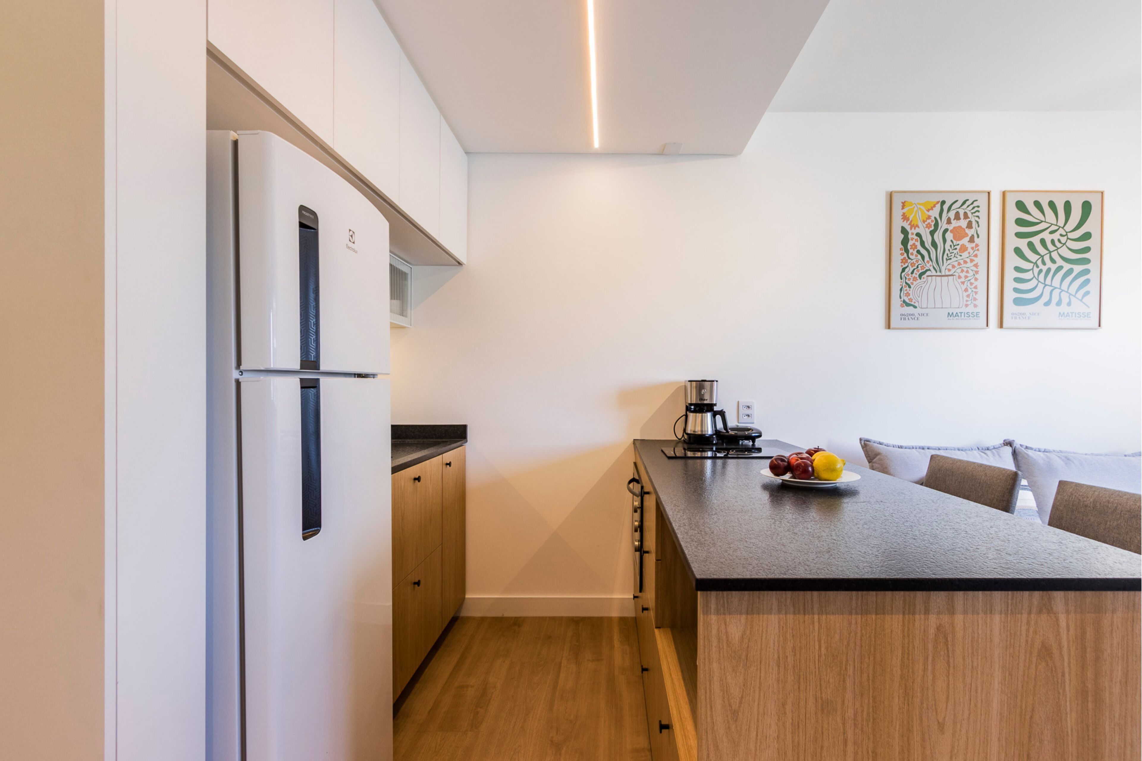 Una cocina compacta con refrigerador, gabinetes de madera, cafetera y un plato de fruta sobre la encimera.
