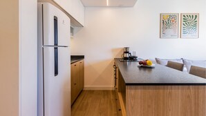 Una cocina compacta con refrigerador, gabinetes de madera, cafetera y un plato de fruta sobre la encimera.