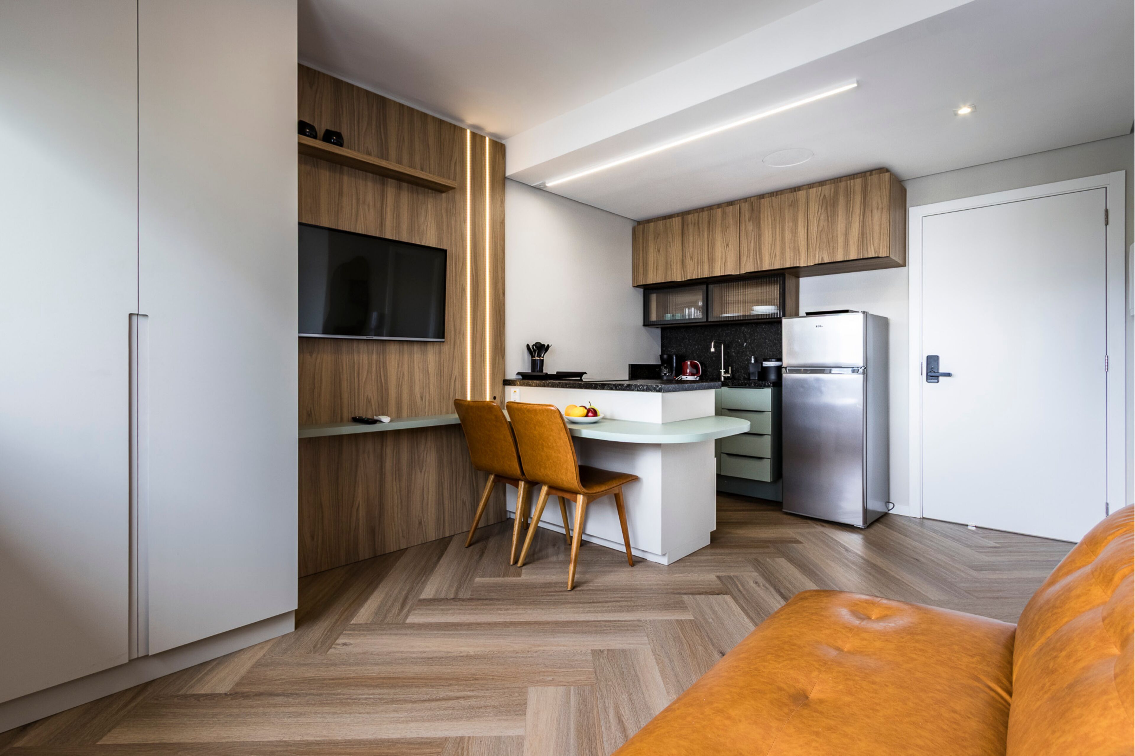 Una cucina moderna con TV integrata, mobili in legno, una zona pranzo con due sedie e un divano.
