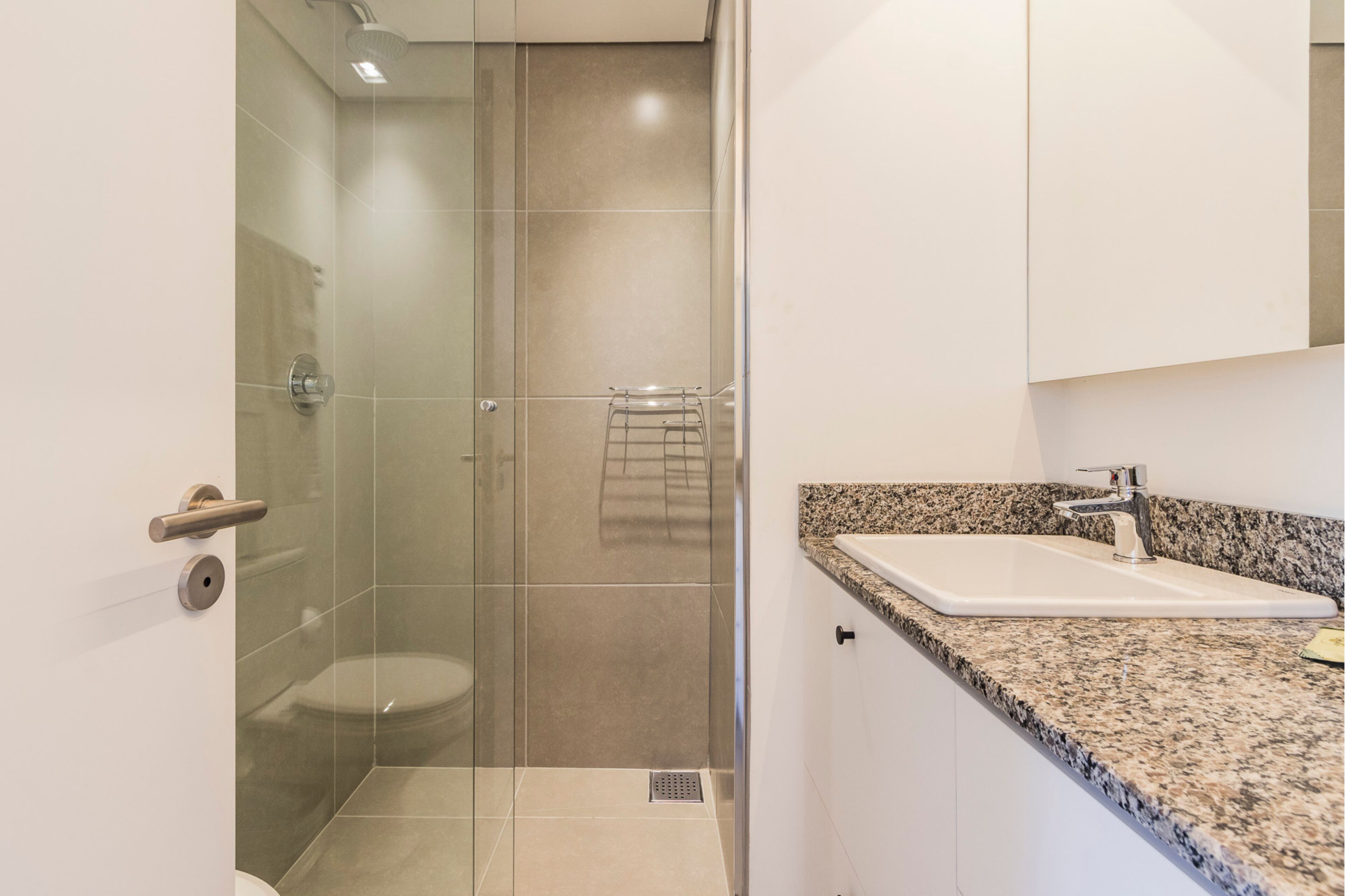 Une salle de bain moderne avec une douche à parois de verre, un lavabo blanc doté d’un plan de travail en granit et un miroir au-dessus du lavabo.