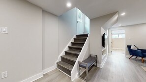 A modern interior with a staircase, a flat-screen TV mounted on the wall, and a blue chair in a living area. - Spacious & Quiet Lower Unit. Mins to Airport/ HWY. 2 Parking Spots. Renovated. (Toronto)