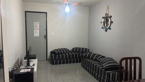 Ein Zimmer mit einer gebogenen Couch, einem Schreibtisch mit Computer und einem Deckenventilator, sowie einer Wanddekoration.