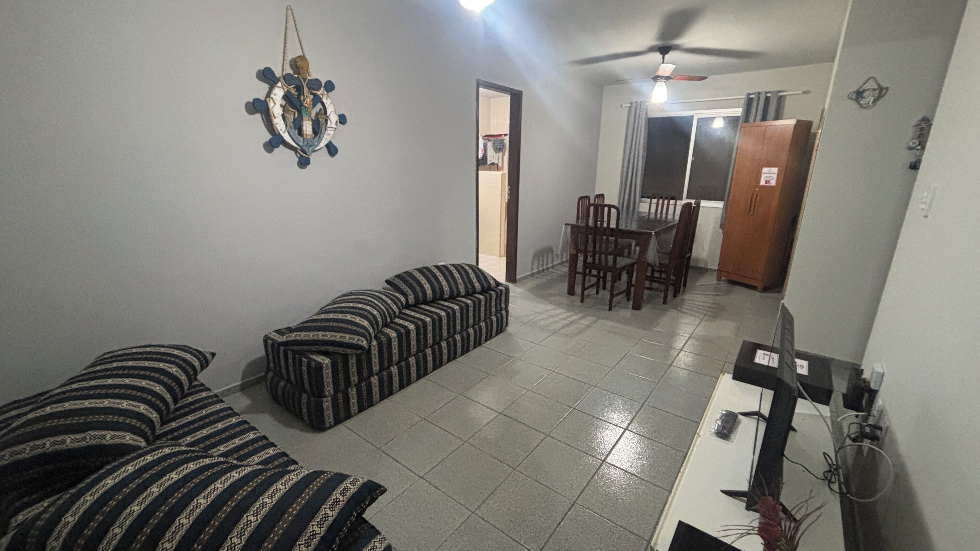 A room with a sofa, a dining table with chairs, and a ceiling fan.