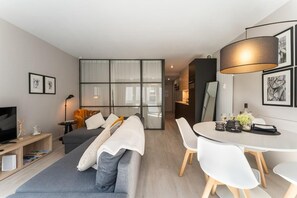 A modern living room with a sofa, a dining table with chairs, a TV, and artwork on the walls. - A stunning, elegant, and bright apartment, ideally located in the heart of the city. (Oostende)