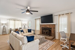 A modern living room with a fireplace, a sofa set, a coffee table, and a ceiling fan. - Cozy 3BR Charlotte Home ~ Backyard Fire Pit (Charlotte)