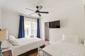 Ett hotellrum med två sängar, en takfläkt, en TV och ett fönster med gardiner.