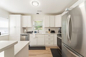 A modern kitchen with white cabinetry, stainless steel appliances, and a window with blinds. - Cozy 3BR Charlotte Home ~ Backyard Fire Pit (Charlotte)