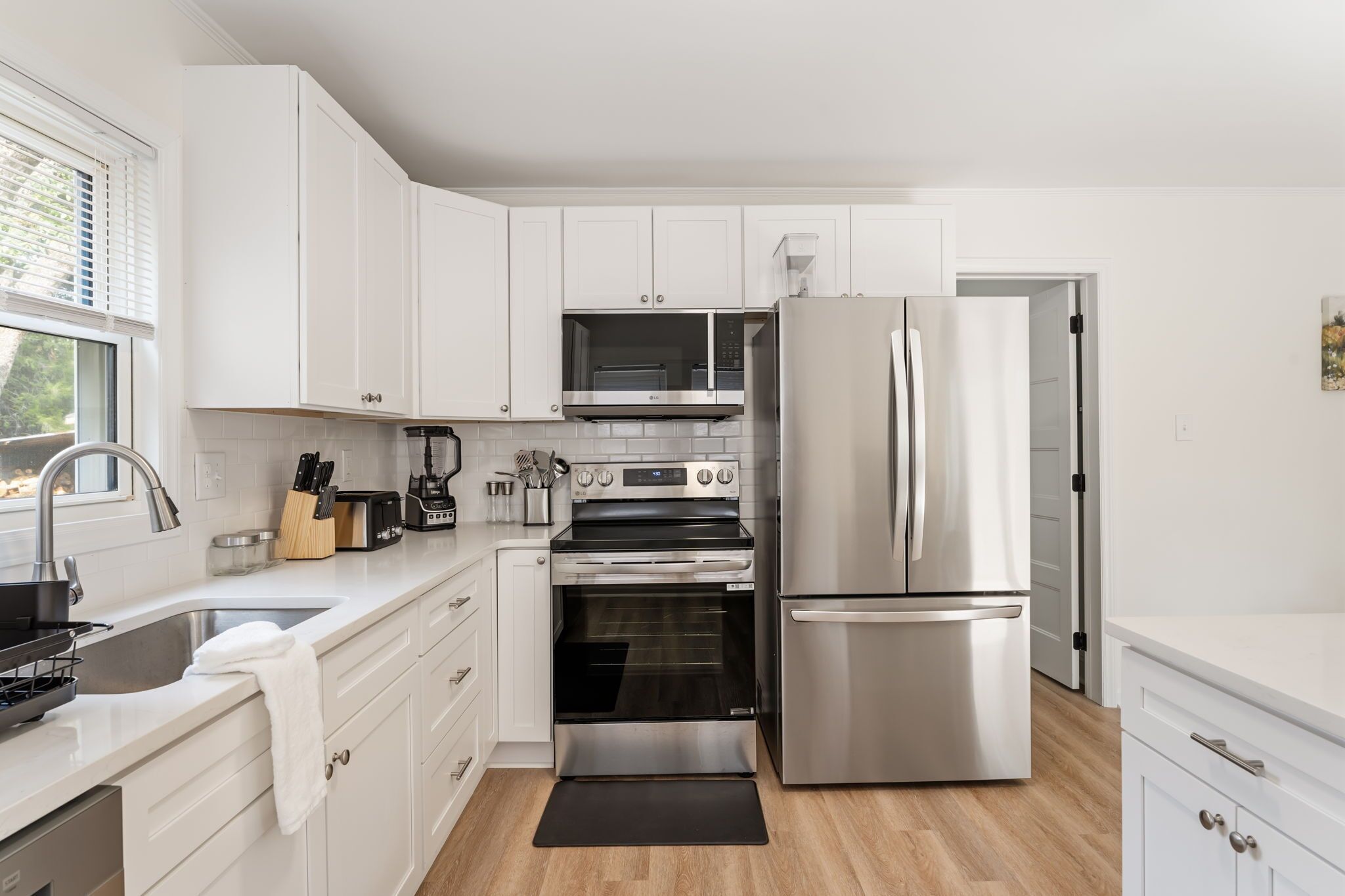 Una cocina moderna con armarios blancos, electrodomésticos de acero inoxidable, horno empotrado y refrigerador.