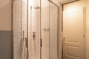 Ducha con cerramiento de vidrio, cabezal de ducha de mano y grifo empotrado.