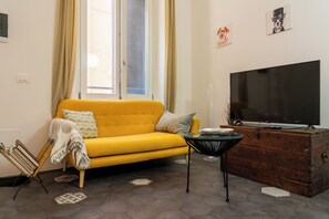 Una sala de estar con un sofá amarillo, un televisor sobre un aparador de madera y una alfombra estampada.