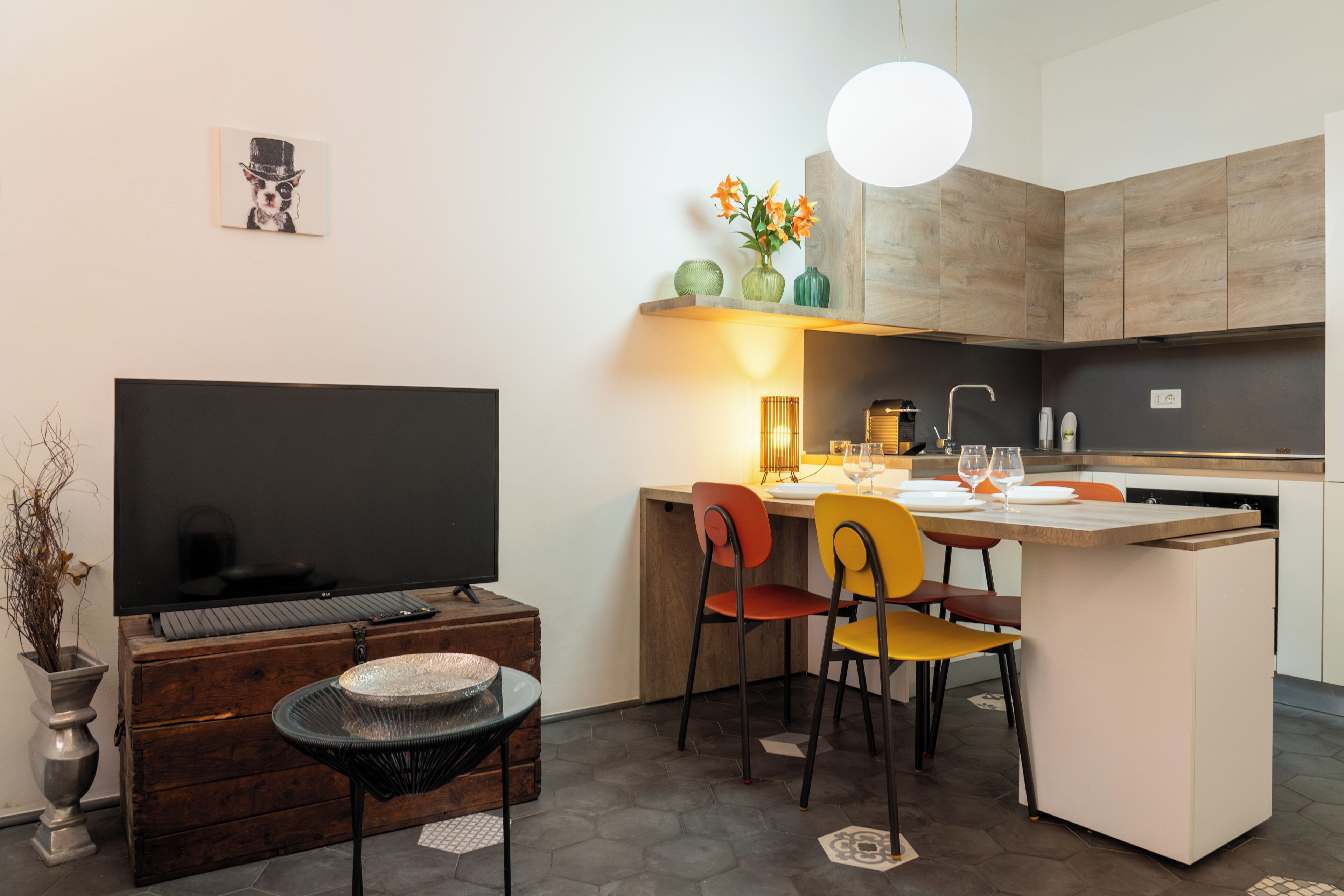 Una cocina moderna con zona de comedor, televisor y un jarrón decorativo con flores.