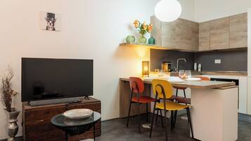 Una cocina moderna con zona de comedor, televisor y un jarrón decorativo con flores.