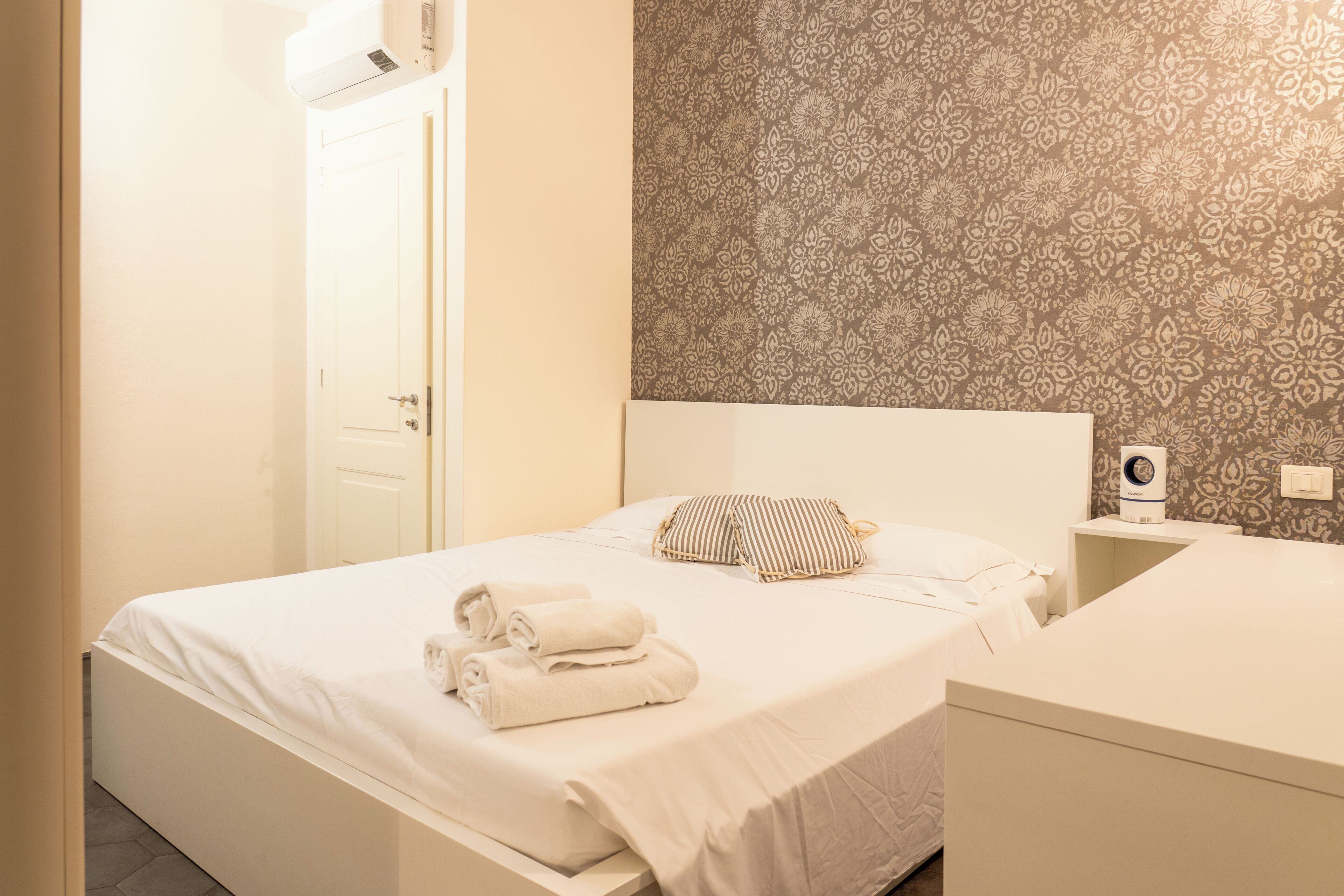 Habitación de hotel con cama, almohadas, una mesita de noche y un diseño decorativo en la pared.