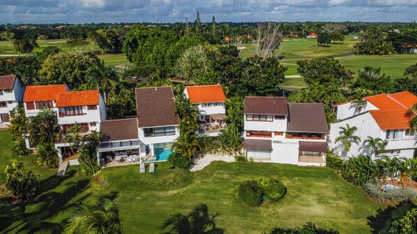 A residential area with houses featuring red roofs, a swimming pool, and lush greenery.