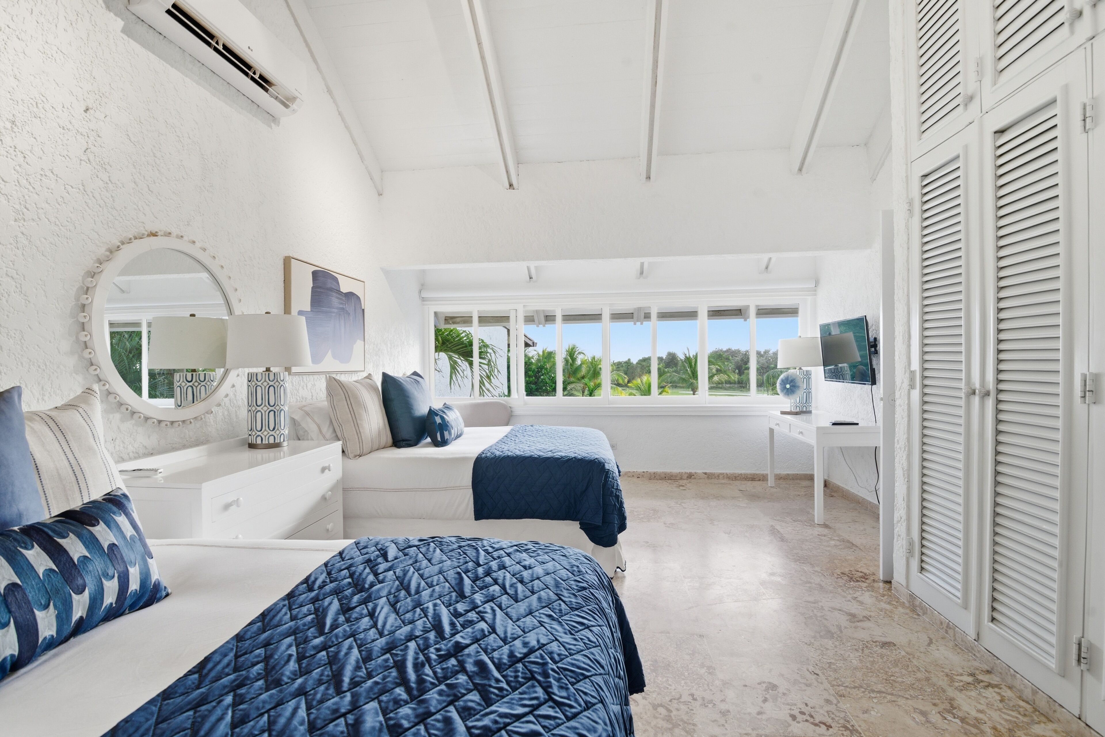 A bedroom with a bed, bedside table, lamp, and a window with a view of greenery.