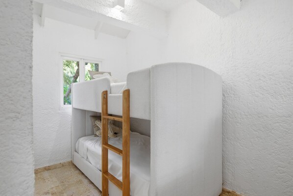 A bunk bed with a ladder, a window with a view of greenery, and a white textured wall.