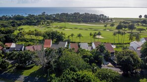 A golf course with a view of the ocean, surrounded by palm trees and houses with red roofs.