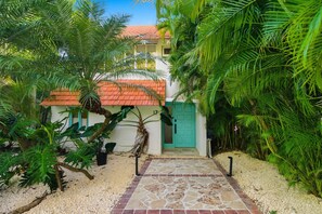 A pathway leading to a building with a tiled roof and a green door, surrounded by lush tropical foliage.