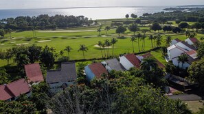 A golf course with a view of the ocean, surrounded by palm trees and buildings with red roofs.