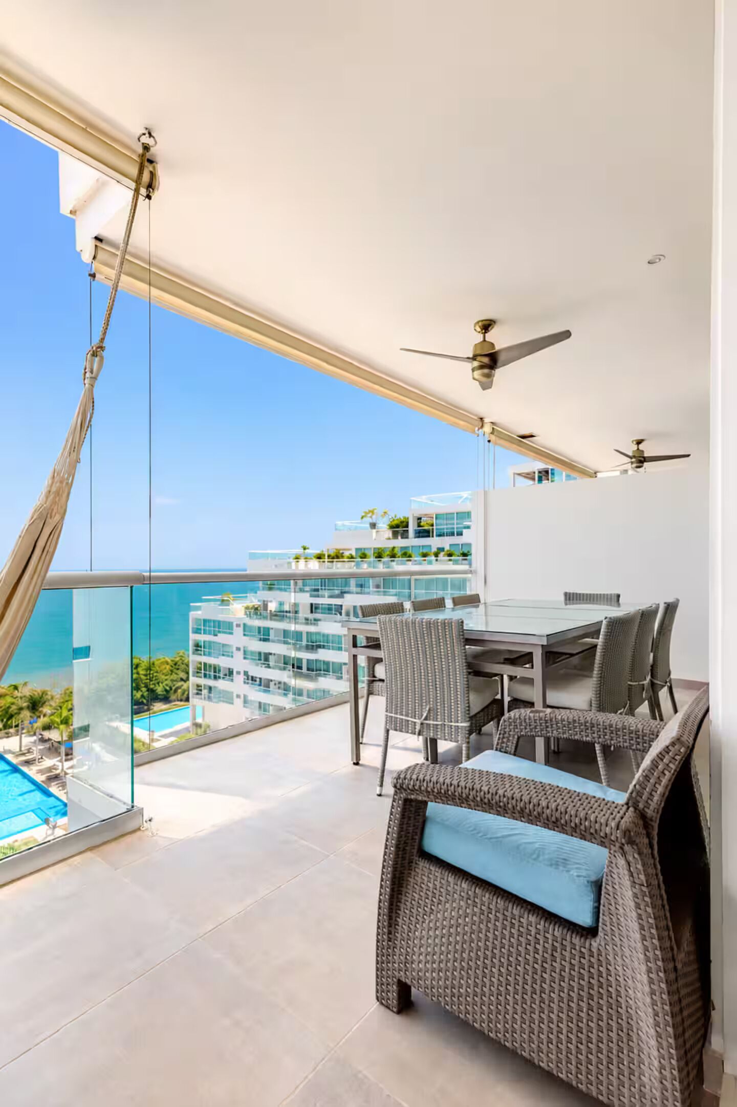 A balcony with a dining table and chairs, a ceiling fan, and a view of a building and the sea.