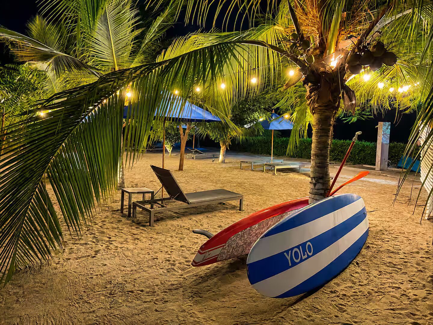 A beach setting with a lounge chair, a surfboard, and palm trees.