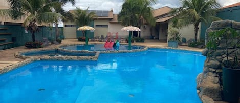 A swimming pool with a stone border, palm trees, and a cloudy sky.
