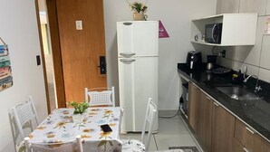 A compact kitchen with a refrigerator, microwave, and sink. There is a dining table with chairs and a small plant on the table.