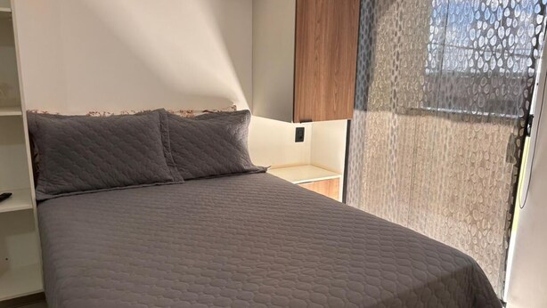 A bed with a quilted cover, a wooden headboard, and a window with a patterned curtain.