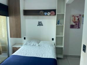 A bedroom with a bed, a nightstand, a built-in shelf with decorative items, and a poster on the wall.