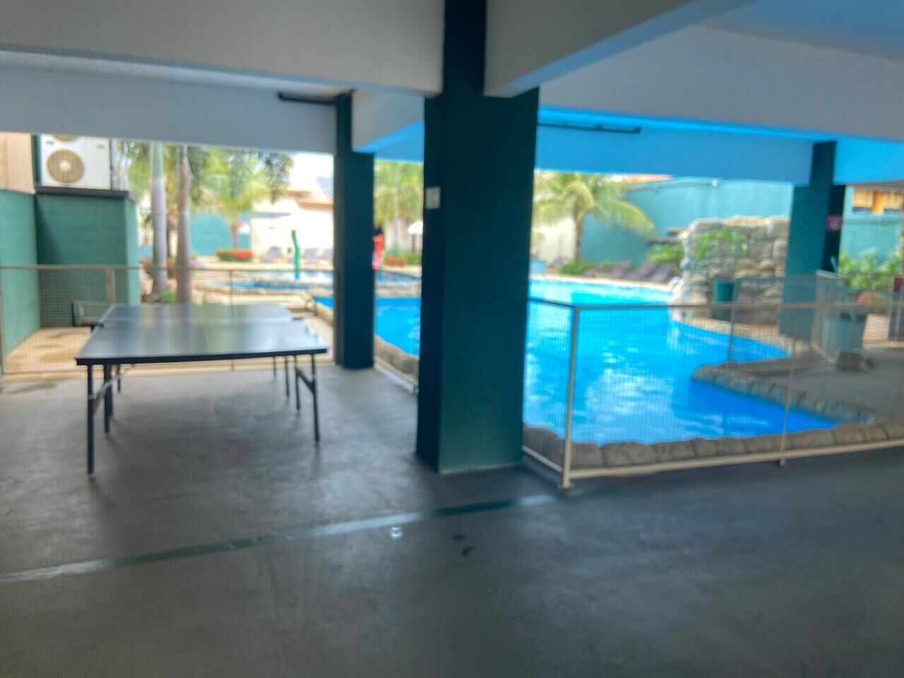 Un área de piscina con mesa y sillas, vista a la piscina y una zona de estar cubierta.