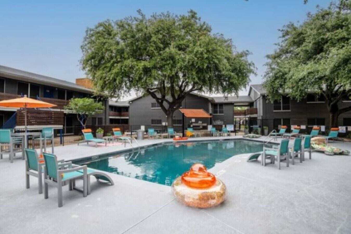 Ein Pool mit Liegestühlen und Sonnenschirmen, umgeben von Bäumen und Gebäuden.
