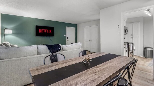 A modern living room with a sofa, a dining table, and a kitchen in the background. - Arlington 2BR | AT&T, Globe Life, 6 Flags, Parking (Arlington)