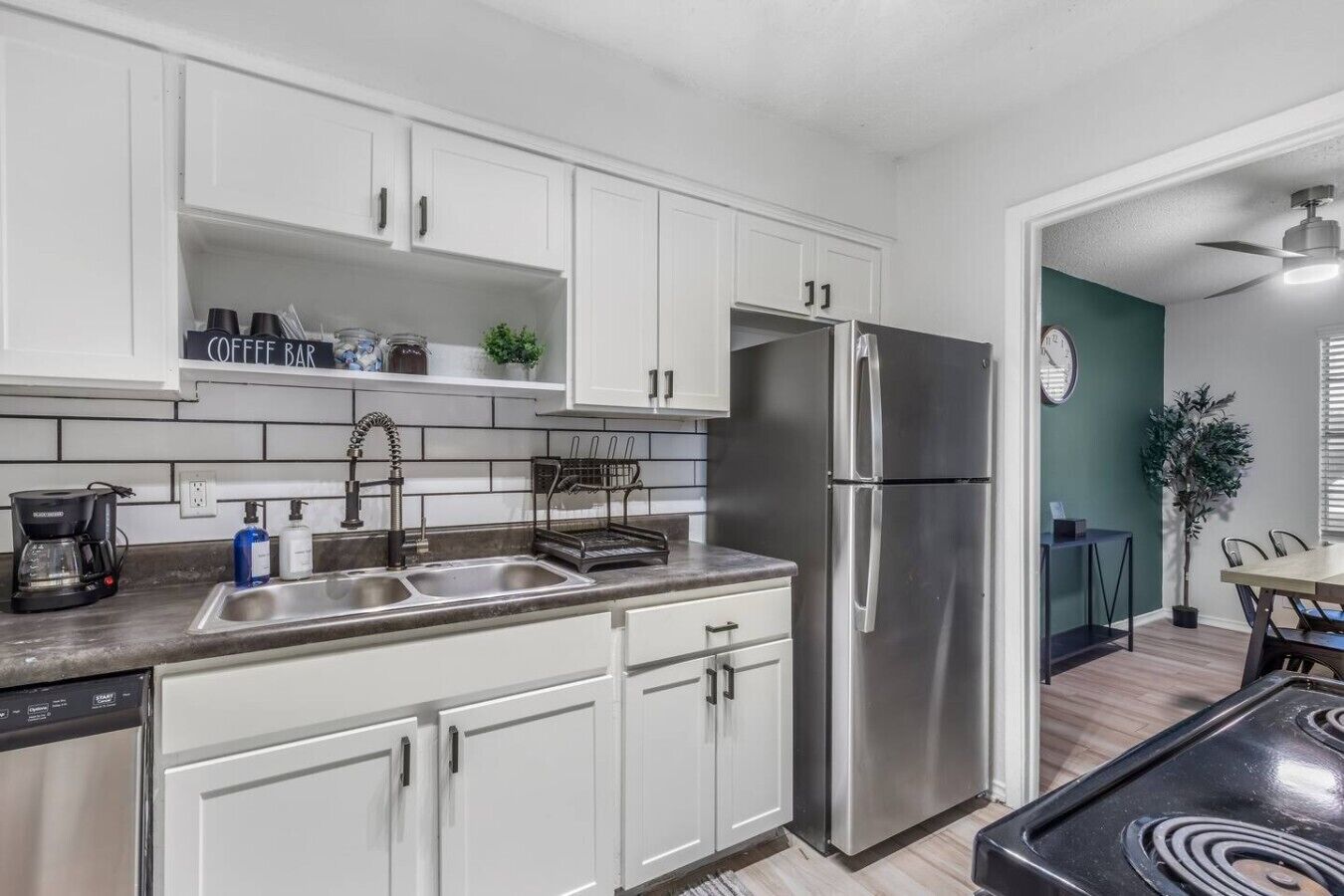 A modern kitchen with white cabinets, stainless steel appliances, a coffee bar, and a dining area with a table and chairs.