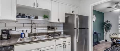 Una cocina moderna con armarios blancos, electrodomésticos de acero inoxidable, una barra de café y un comedor con mesa y sillas.