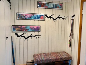 A room with a wooden wall, a bench, and two framed artworks. - Where the lakes meet the mountains. (Thornton)