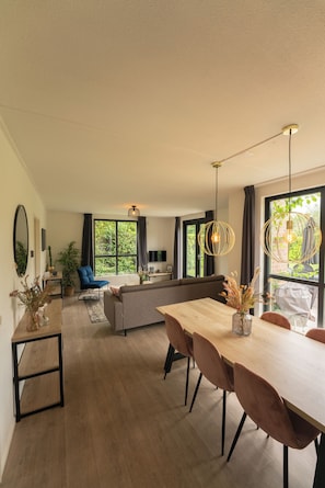A modern living space with a dining area, a sofa, and a large window providing a view of greenery.