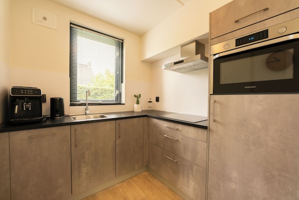 A modern kitchen with a built-in oven, a coffee maker, and a window with blinds.