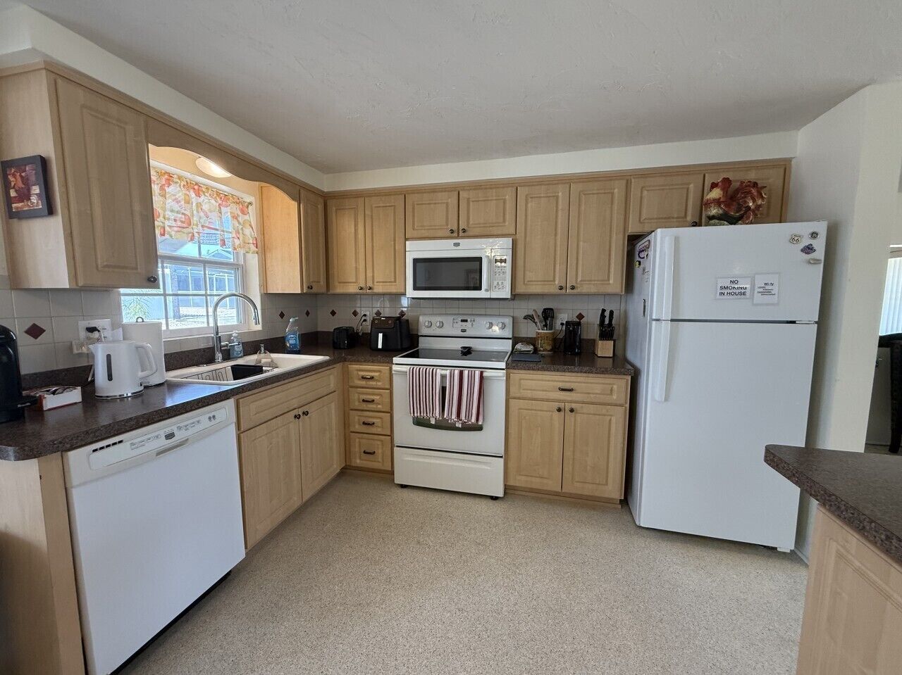 A kitchen with wooden cabinets, a white stove, a microwave, and a refrigerator.