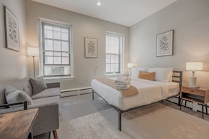 A modern bedroom with a bed, bedside tables, a sofa, and large windows. - Back Bay Area Elegant Studio Apt (Boston)