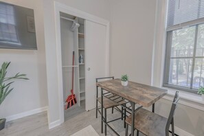 A dining area with a wooden table and chairs, a potted plant, and a closet with a mop. - Back Bay Area Elegant Studio Apt (Boston)