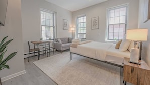 Een moderne slaapkamer met een bed, nachtkastje, lamp en een klein bureau met een stoel.