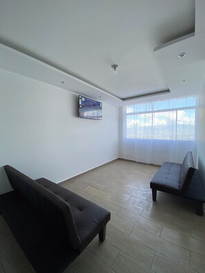 Ein geräumiger Raum mit großem Fenster, einem an der Wand befestigten Flachbildfernseher und zwei dunkelgrauen Sofas.