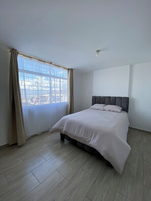 Ein Schlafzimmer mit einem Bett, einem Fenster mit Vorhängen und Blick auf Gebäude.