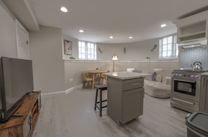 A compact kitchen with a dining area, a built-in oven, and a TV on a wooden stand. - Spacious & Modern 1 Bedroom | Back Bay (Boston)