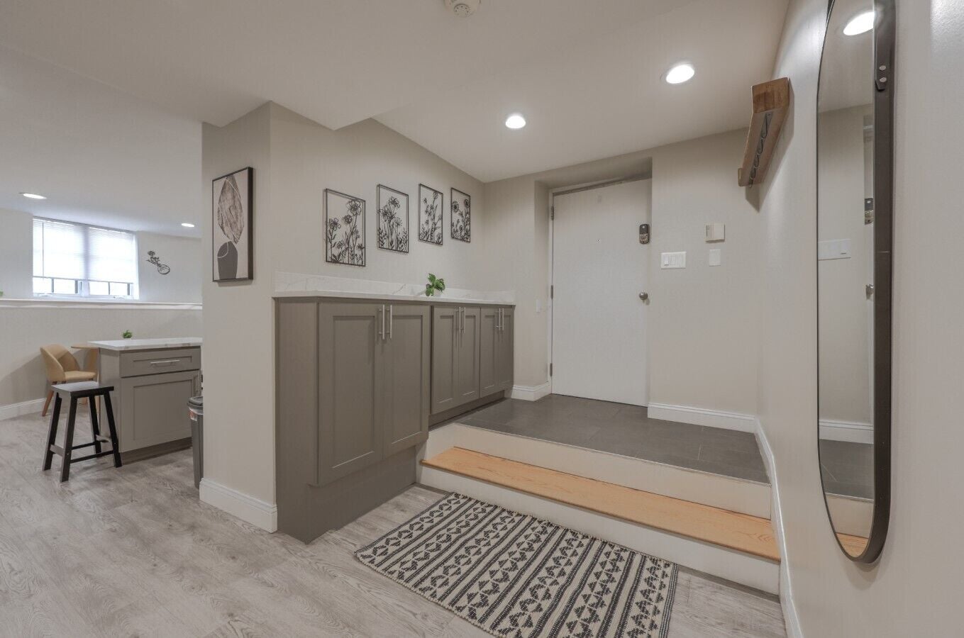 A modern kitchen with grey cabinets, a white countertop, and a small stool.